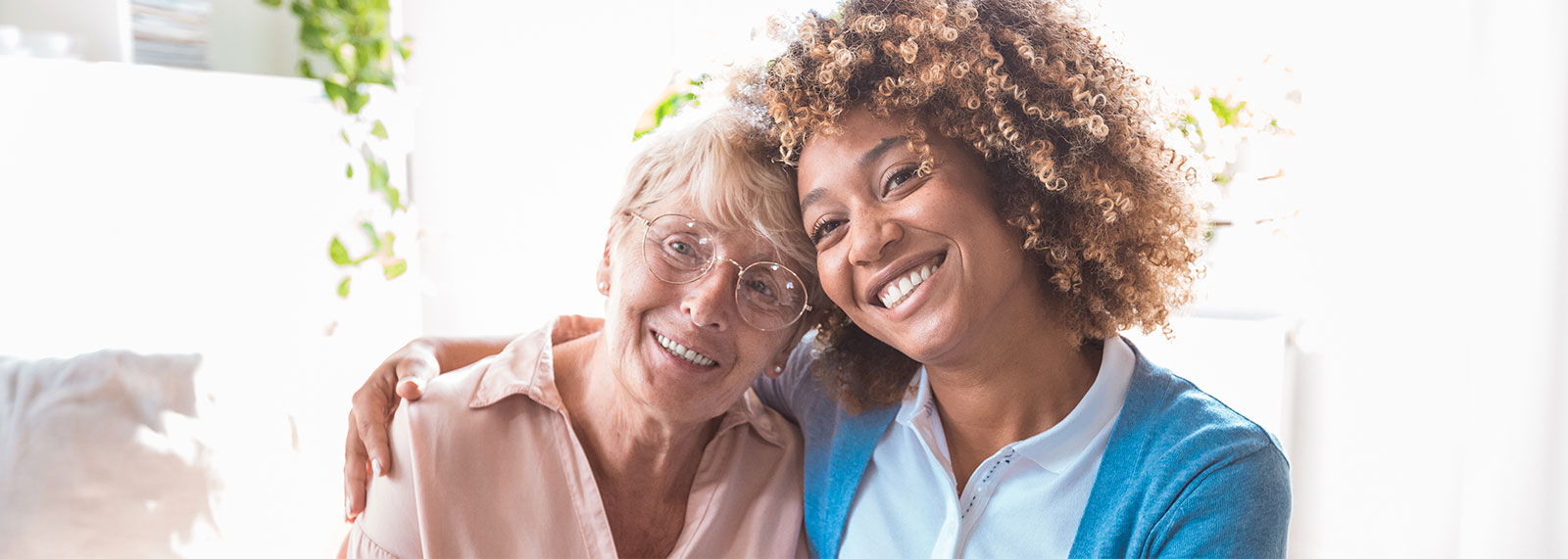 caregiver with her arm around a senior woman's shoulders smiling for the camera